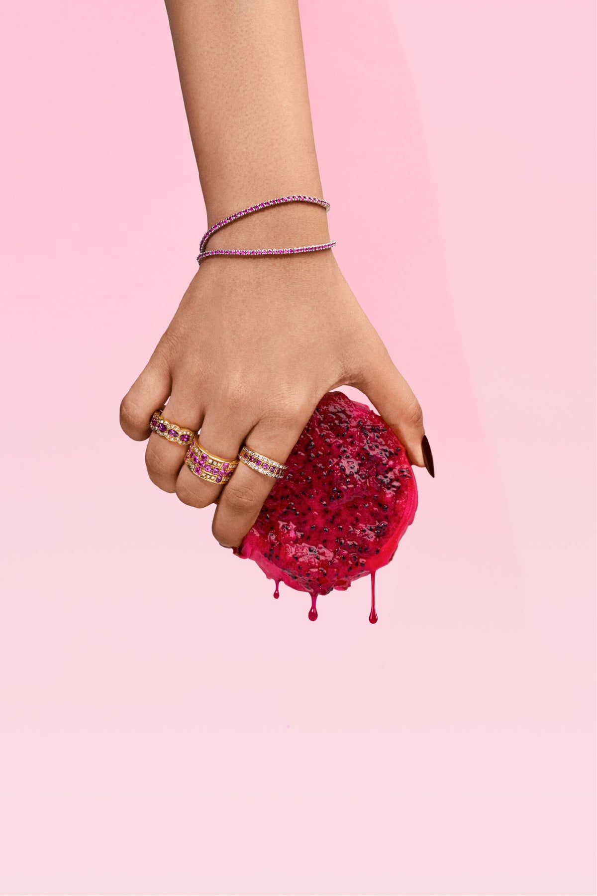 Hand wearing rings and bracelets holding a red fruit