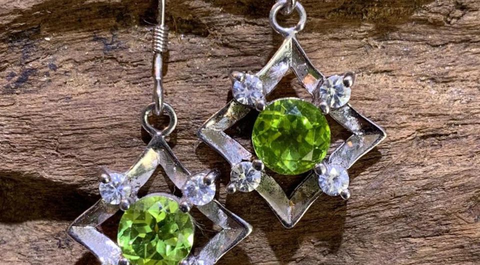 Green gemstone drop earrings resting on weathered wood