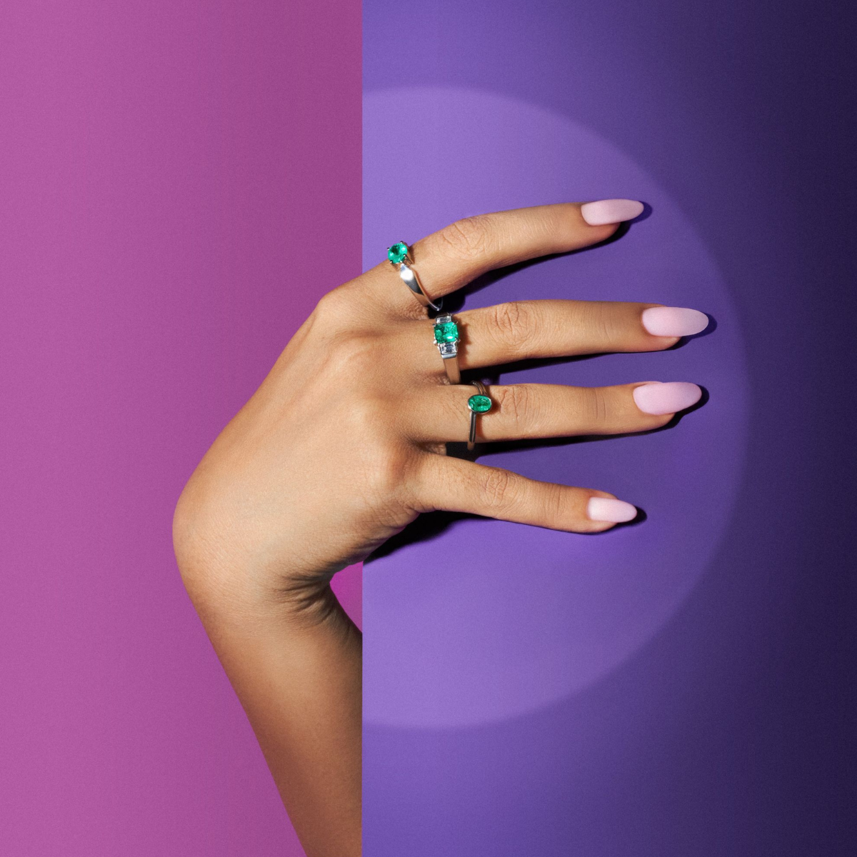 Hand wearing green gemstone rings against a violet backdrop